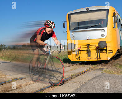 Cycliste est terrifié par le train avant de se précipiter sur les voies. Choqué biker ride un passage à niveau à l'avant d'un train qui approche. Banque D'Images