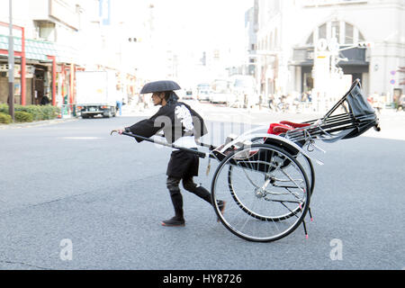 Japon, Tokyo, 18 novembre 2016, conducteur de pousse-pousse en costume traditionnel tirant une charrette dans la rue. Jinrikisha pilote ne fonctionne avec panier vide sur route, Tokyo, Banque D'Images