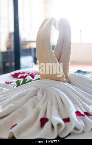 Les oiseaux de décoration avec des pétales de rose rouge sur blanc nettoyer lit dans chambre d'hôtel avec rétro-éclairage. Banque D'Images