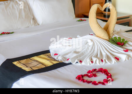 Les oiseaux de décoration avec des pétales de rose rouge sur blanc nettoyer lit dans chambre d'hôtel. Banque D'Images