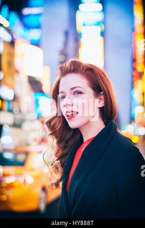 Les jeunes femmes en robe rouge et manteau noir saluant un taxi à Times Square New York Banque D'Images