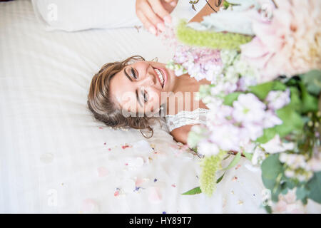 Une fiancée portant sur lit dans sa suite nuptiale tout en maintenant un bouquet de fleurs Banque D'Images