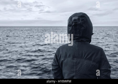 Personne à capuchon sans visage à la distance à l'horizon en plus de l'eau de mer sur journée d'hiver froides et venteuses, d'anticiper l'avenir imprévisible Banque D'Images