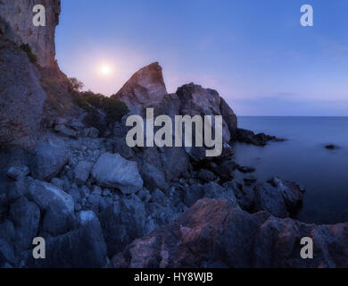 Paysage de montagne sur la mer la nuit. De hautes roches et les pierres dans l'eau sur le fond de ciel bleu nuit avec la pleine lune en été. Sur scène étonnante Banque D'Images