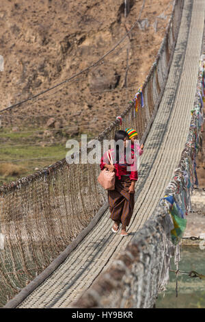 Une mère avec son bébé sur son dos traverse le long pont suspendu au-dessus de la Pho Chhu, près de Punakha, Bhoutan. Banque D'Images