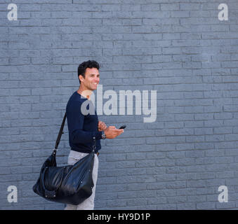 Portrait de côté un homme séduisant la marche avec sac et téléphone mobile Banque D'Images