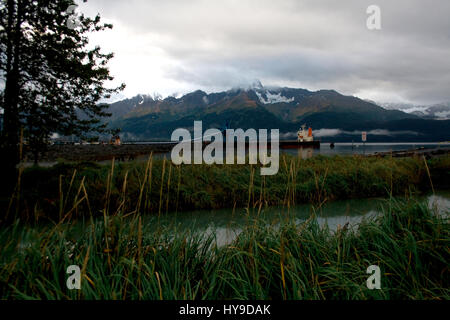 Un paysage avec des montagnes et de l'herbe dans Seward, Alaska avec un bateau d'être chargé de charbon dans la distance. Banque D'Images