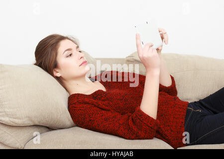 Joyeux belle jeune fille rousse dans une veste jeans bleu assis sur le canapé à la maison et parler au téléphone cellulaire. Banque D'Images