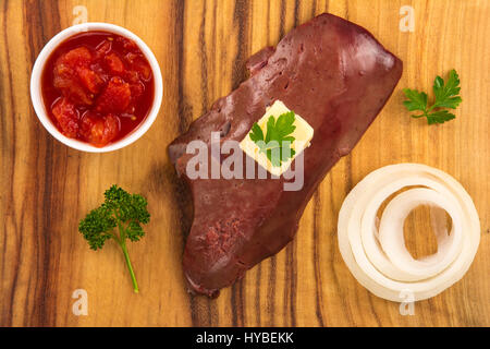 Portrait d'un foie de veau cru sur planche de bois avec du beurre, l'oignon, la tomate et le persil dés Banque D'Images