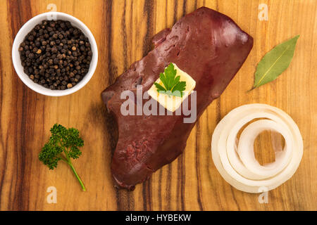 Portrait d'un foie de veau cru sur planche de bois avec du beurre, l'oignon, le poivre noir, le laurier et le persil Banque D'Images