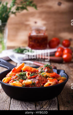 Meatball avec pâtes penne avec sauce rouge épicée dans la poêle en fonte sur table en bois en milieu rural Banque D'Images