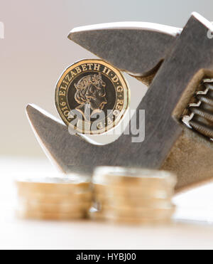 Nouveau livre €1 coin tenue à une clé réglable sur fond clair avec des pièces empilées dans l'avant-plan montrant un squeeze sur les finances Banque D'Images