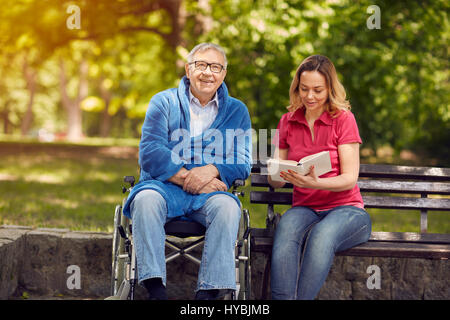 Passer du temps ensemble en plein air livre lecture fille gaie et souriant mobilité père en fauteuil roulant Banque D'Images