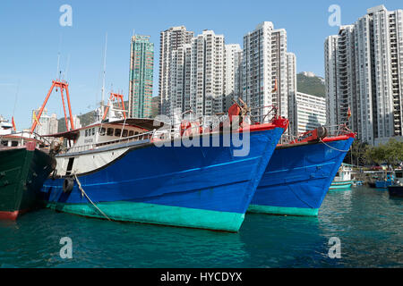 La pêche commerciale peint de couleurs vives, des bateaux amarrés dans le canal d'Aberdeen, des tours d'habitation sur l'île de Hong Kong derrière. Banque D'Images