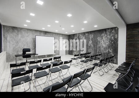 Prix pour les cours avec beaucoup de chaises. Les murs sont blanc, intérieur loft. Sur la droite il y a une porte. Sur l'arrière-plan il y a une table avec un ordinateur portable. Banque D'Images