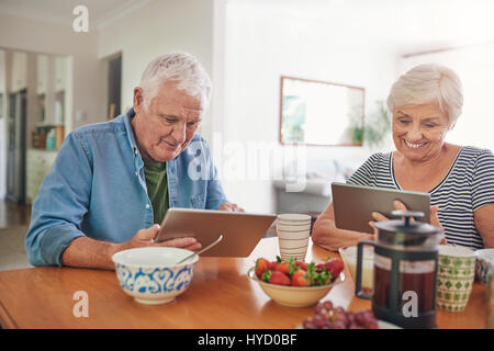 Smiling seniors à l'aide de tablettes numériques pendant le petit-déjeuner à la maison Banque D'Images