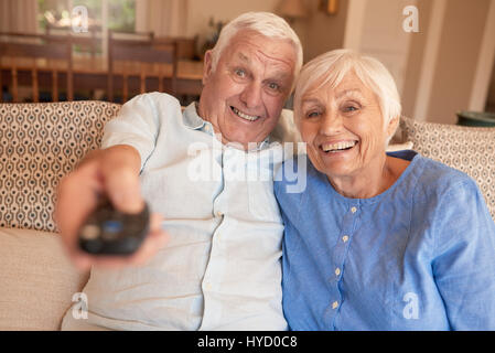 Happy senior couple regardent la télévision ensemble sur leur canapé Banque D'Images