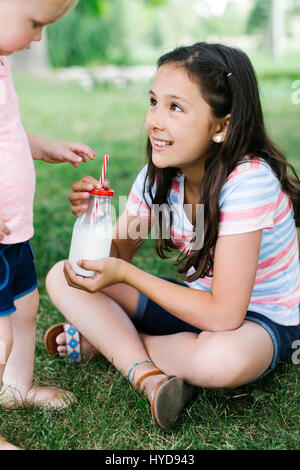 Fille (10-11) partageant une bouteille de lait avec sa sœur (2-3) stationnement Banque D'Images