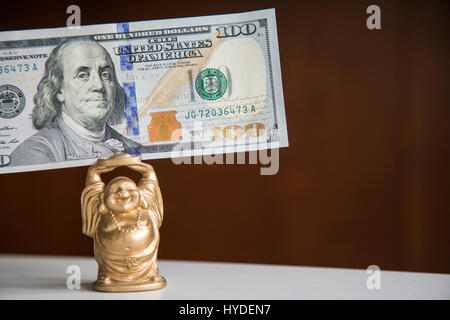 Un petit Bouddha en or du prince est titulaire d'un cent de dollar, monnaie d'entre nous au-dessus de sa tête Banque D'Images