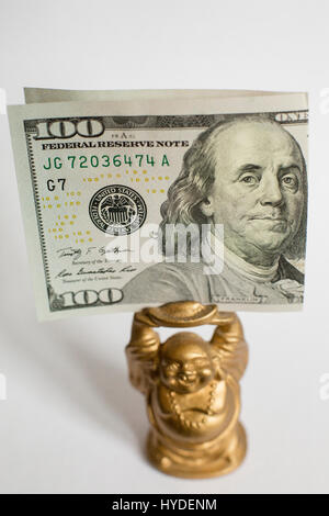 Un petit Bouddha en or du prince est titulaire d'un cent de dollar, monnaie d'entre nous au-dessus de sa tête Banque D'Images