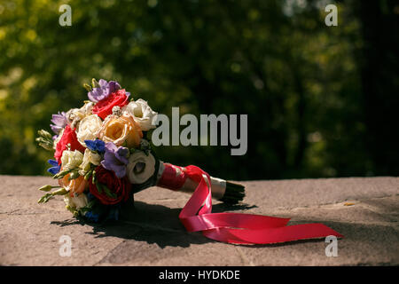 Bouquet de mariage coloré avec ruban rose, allongé sur la pierre Banque D'Images