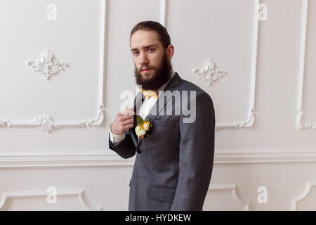 Fort beau barbu, brutal groom posing in suit avec orange noeud sur un fond clair Banque D'Images