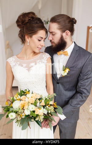 Portrait d'une belle épouse avec un bouquet et le marié avec une barbe dans un intérieur clair Banque D'Images