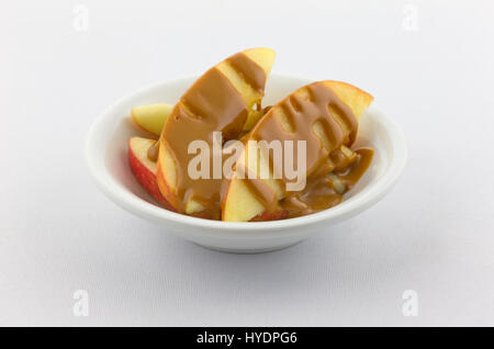 Tranches de pommes rouges couvertes de beurre d'arachides crémeux dans un petit bol au-dessus d'une nappe blanche. Banque D'Images