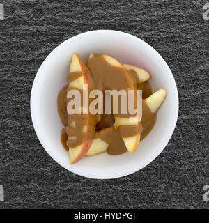 Tranches de pommes rouges couvertes de beurre d'arachides crémeux dans un petit bol au-dessus d'une table d'ardoise noire. Banque D'Images