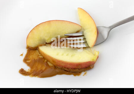 Trois tranches de pomme rouge sur une plaque blanche avec du beurre d'arachide et d'une fourchette. Banque D'Images