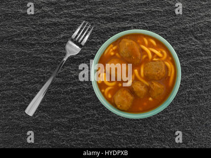 Vue de dessus d'une portion de spaghetti et boulettes de viande dans un bol avec une fourchette pour le côté au-dessus d'une table d'ardoise noire. Banque D'Images