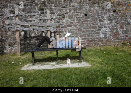 Femme allongée sur un banc de la lecture au soleil, la fête du livre, Laugharne, au Pays de Galles Banque D'Images