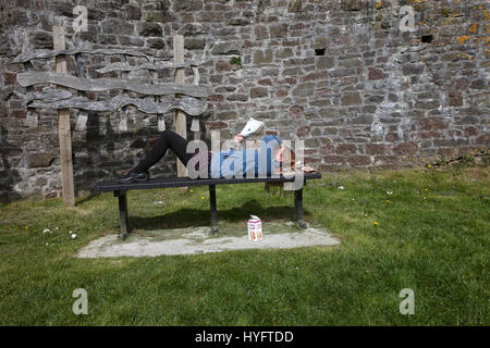 Femme allongée sur un banc de la lecture au soleil, la fête du livre, Laugharne, au Pays de Galles Banque D'Images