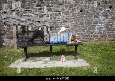 Femme allongée sur un banc de la lecture au soleil, la fête du livre, Laugharne, au Pays de Galles Banque D'Images