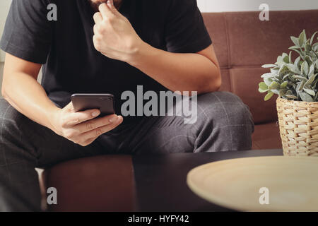 L'homme créateur la main à l'aide de smart phon pour paiements mobiles,vente en ligne,canal omni sitting on sofa in living room,vase en bois et rotin avec des t Banque D'Images