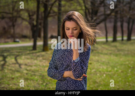 Une fille se tient dans le parc pendant une journée de printemps ensoleillée. Ses cheveux sont en volant dans le vent. Banque D'Images