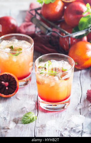 Cocktail avec alcool Tequila Sunrise, orange rouge et glace menthe sur fond blanc en bois Banque D'Images