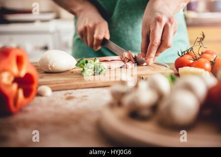 Woman slicing salami sur une planche à découper à la cuisine Banque D'Images