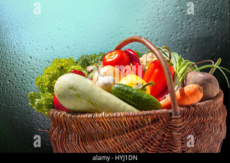 Légumes frais colorés dans panier en osier sur fond vert sombre Banque D'Images