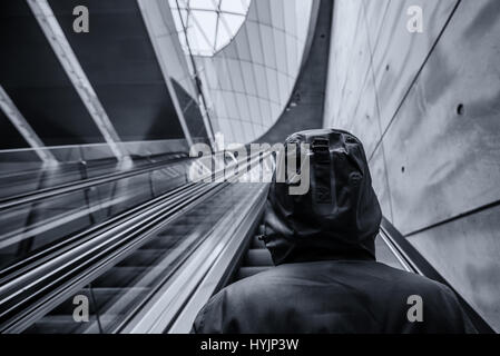 Personne à capuchon méconnaissable sur déménagement dans l'escalator intérieur urbain moderne entourant,image monochromatique avec selective focus Banque D'Images