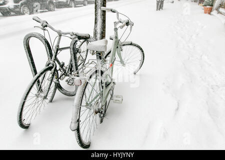 Deux bicyles enchaînés à un rack à l'extérieur sont couvertes de neige pendant une chute de neige à Manhattan. Banque D'Images