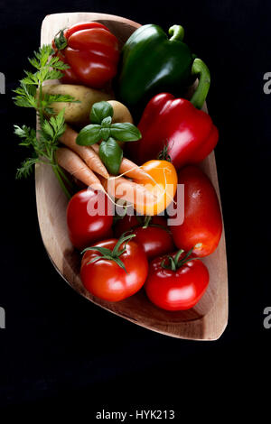 Les légumes d'un véritable bois naturel fait main rectangulaire bol - tomates, carottes, poivrons, pommes de terre - vue du sommet et fond noir Banque D'Images