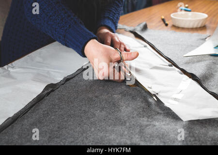 Mains de couturière de couper un tissu gris avec des ciseaux à l'aide d'un gabarit papier Banque D'Images