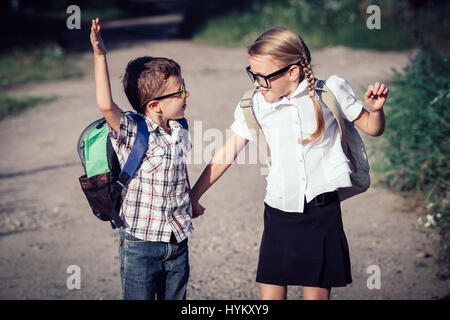 Smiling young school enfants dans un uniforme scolaire sauter sur la route, à la journée. Le concept d'enfants sont prêts à aller à l'école. Banque D'Images