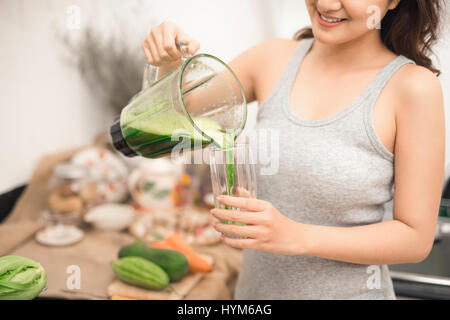 Smiling asian woman making smoothie avec des légumes frais dans le bol mélangeur dans la cuisine à la maison. Banque D'Images