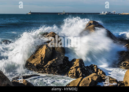 Smashing vagues contre des rochers sur la plage à Nevogilde paroisse civile de Porto, au Portugal. Port de Leixoes sur fond de brise-lames Banque D'Images