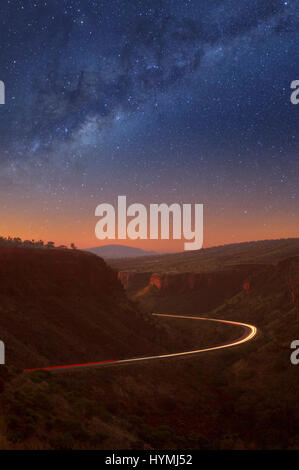 Ciel nocturne et Milky Way, à l'Est Munjina Gorge, dans la région de Pilbara en Australie-Occidentale. Trois trains routiers sont sur la route faisant la lumière des sentiers. Banque D'Images