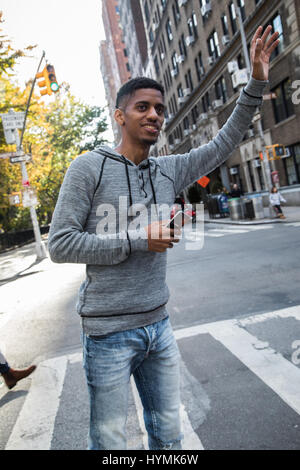 Un portrait d'un jeune homme heureux, saluant un taxi à New York. Tourné au cours de l'automne 2016. Banque D'Images