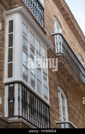 Détail d'un balcon et de grandes fenêtres sur le temps du xixe siècle, rue étroite à l'architecture traditionnelle à Cadix, Espagne Banque D'Images