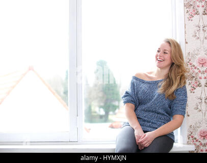 Portrait of a smiling woman sitting next à la fenêtre à la maison Banque D'Images